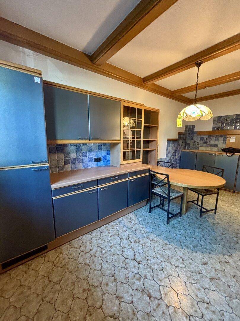 Einbauküche mit dunklen Schränken, Kühlschrank und Essbereich unter Holzbalkendecke.