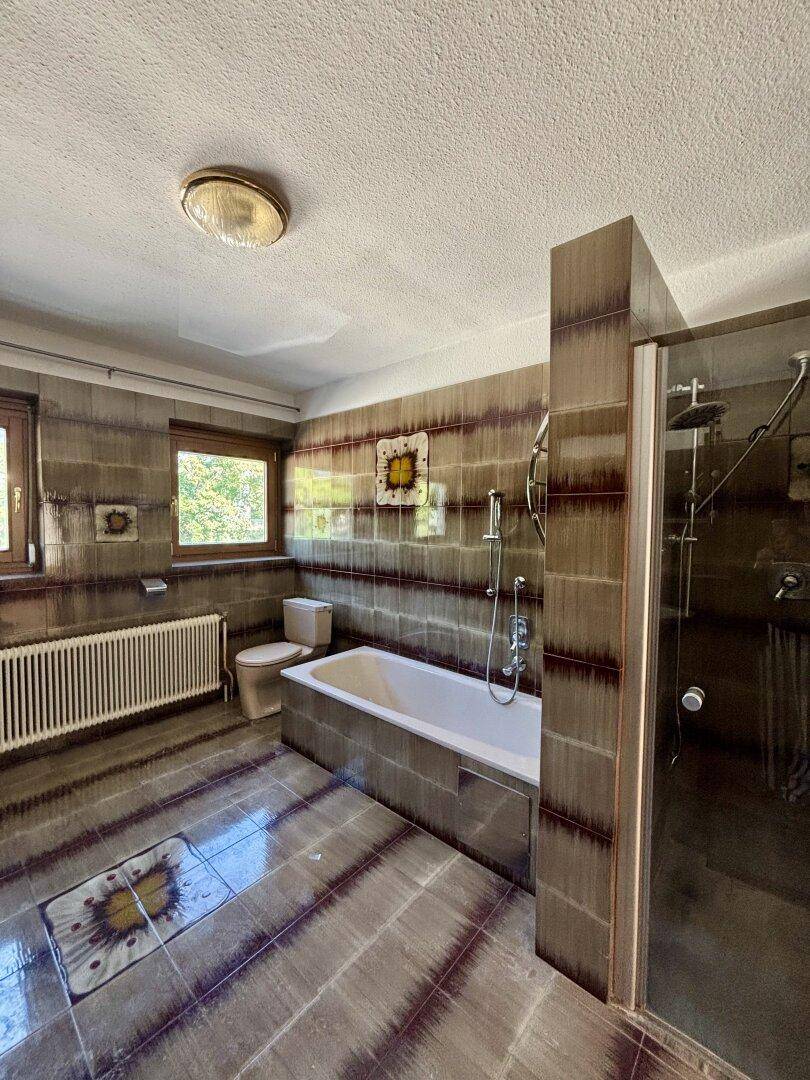 Badezimmer mit Badewanne, Duschkabine, WC und Fenster.