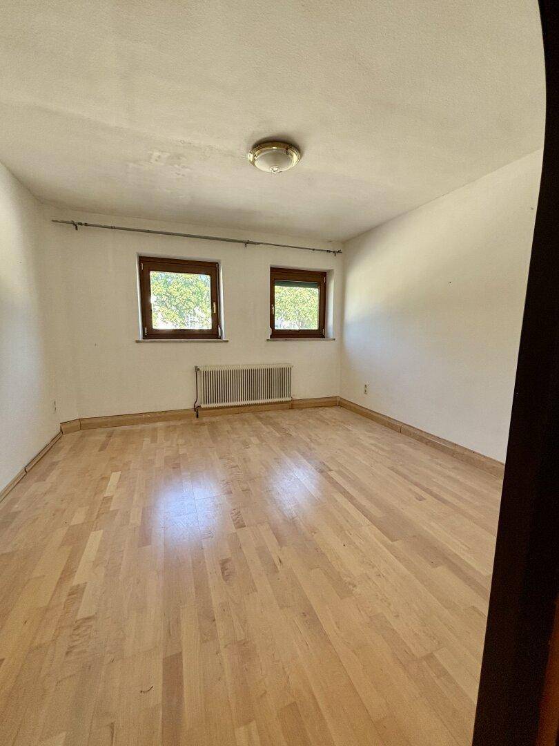 Helles Schlafzimmer mit Parkettboden, zwei Fenstern und Heizkörper.