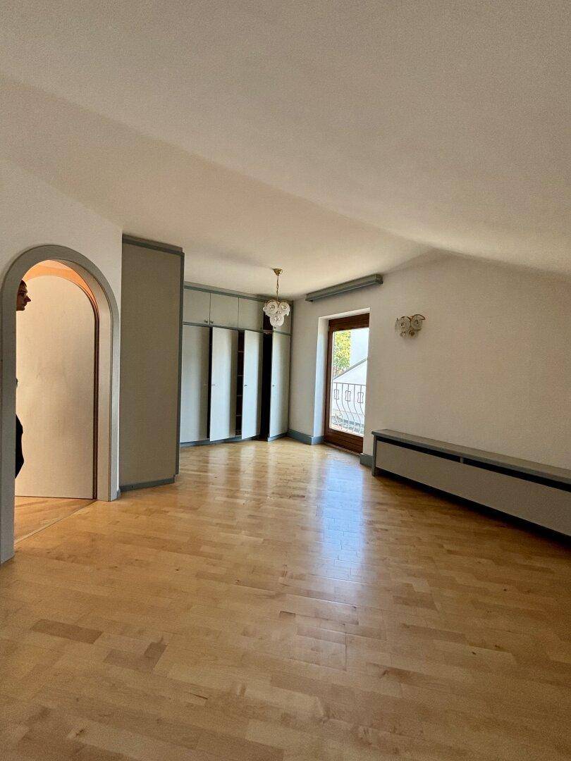 Dachgeschosszimmer mit Parkettboden, Einbauschränken und Zugang zu einem französischen Balkon.
