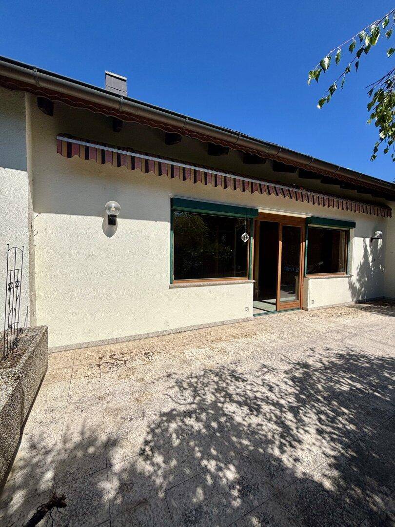 Große gepflasterte Terrasse am Haus mit Markise und viel Sonnenlicht.