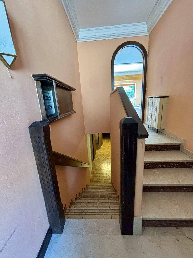 Traditionelles Treppenhaus mit Terrazzostufen, Holzgeländer und pastellfarbenen Wänden.