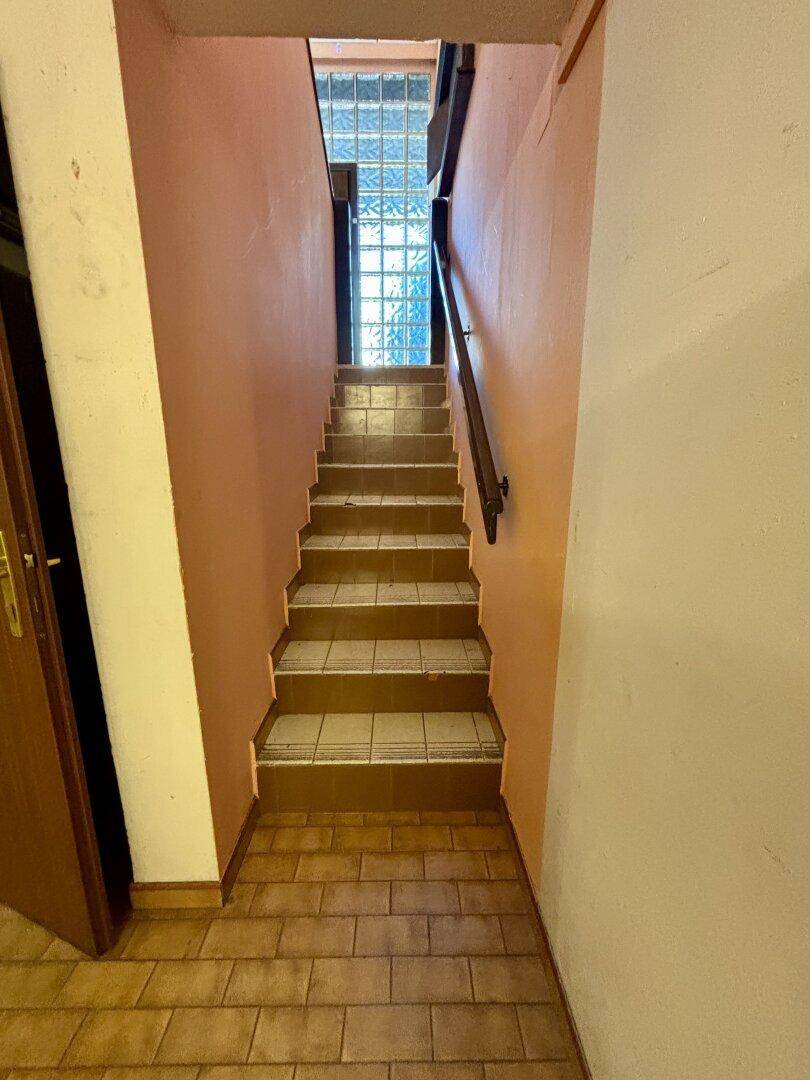 Treppenaufgang mit Fliesenboden und einer Wand aus Glasbausteinen für natürliches Licht.