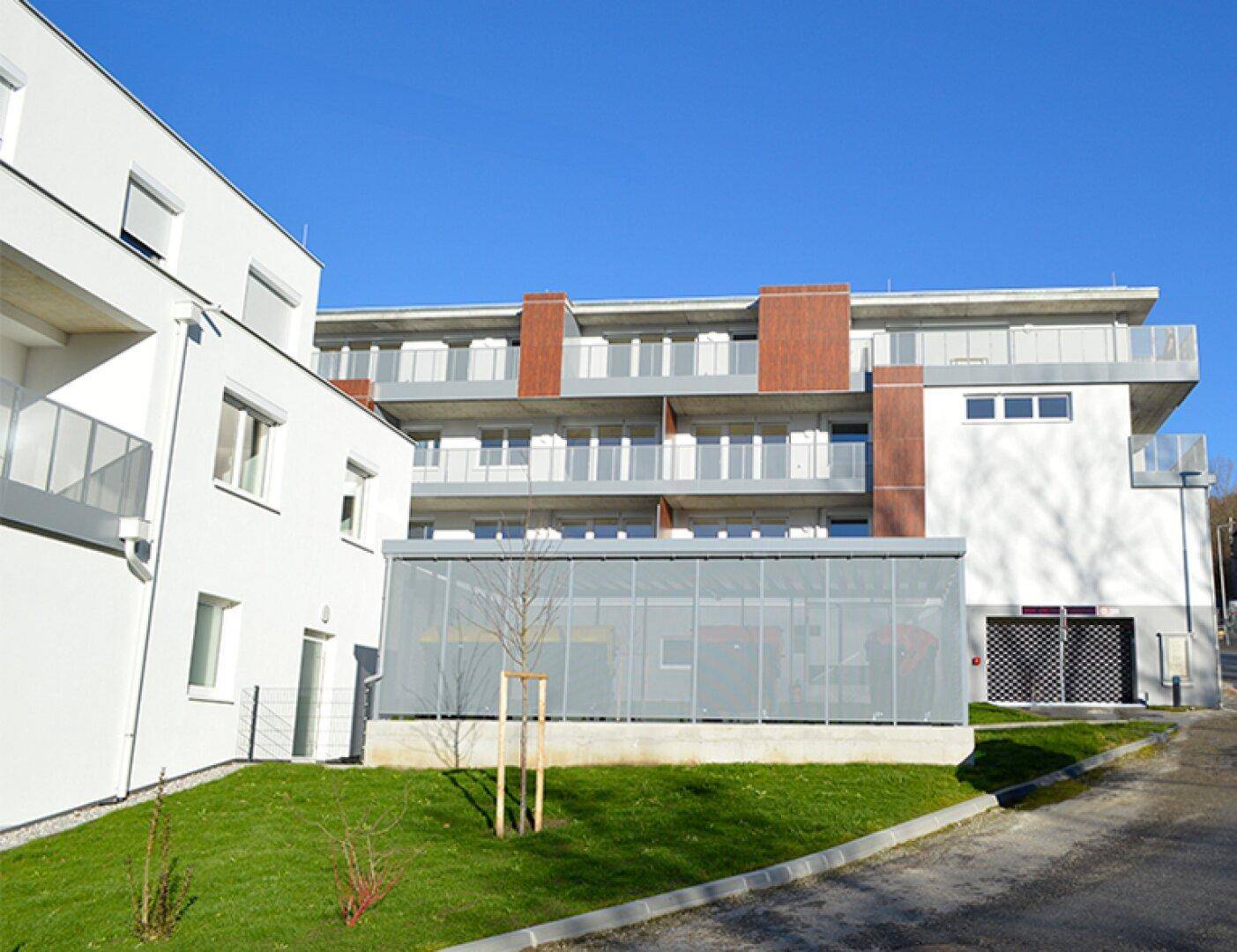 Ansicht der modernen Wohngebäude mit Balkonen und gepflegten Grünflächen unter blauem Himmel.