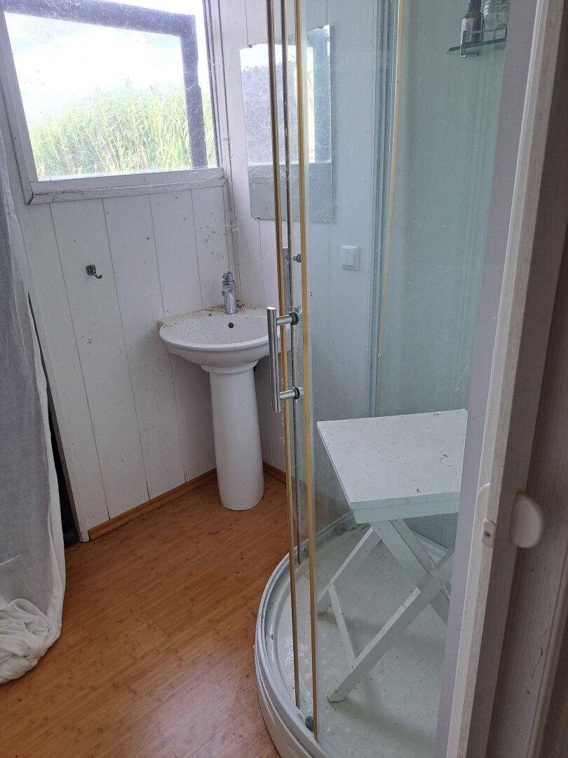 Kleines Badezimmer mit Duschkabine, Standwaschbecken und einem Fenster mit Blick ins Grüne.