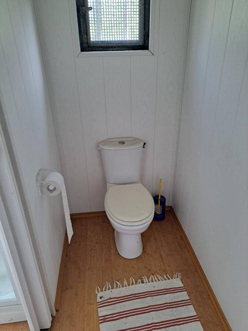 Einfaches WC mit Toilette und einem kleinen Fenster, ausgestattet mit Holzfußboden.