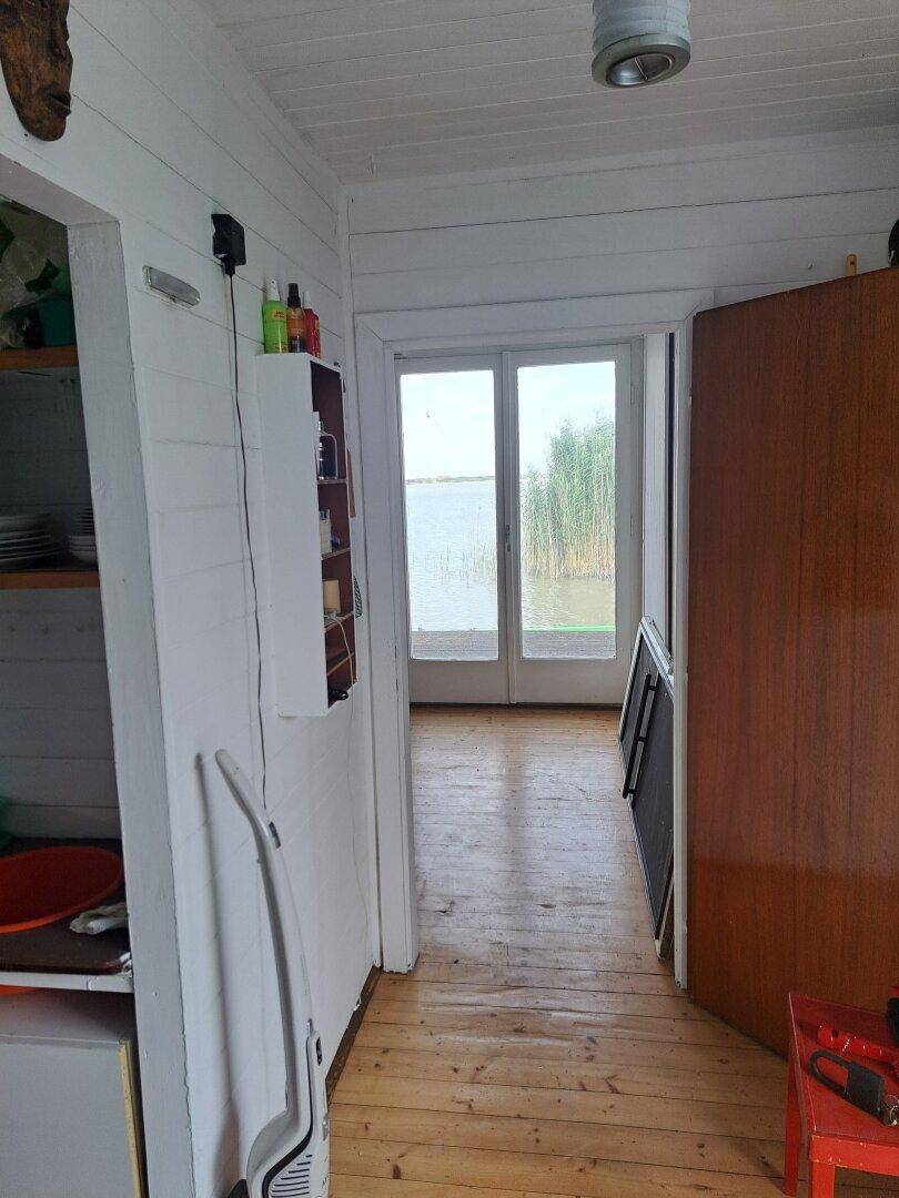 Heller Flur mit Holzdielenboden, der zu Glastüren mit Seeblick und Schilf führt.