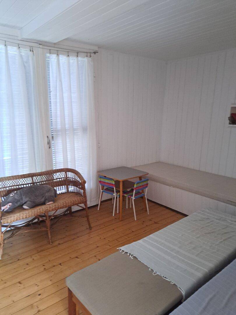 Schlafbereich mit mehreren Schlafgelegenheiten, einem Korbsessel und Holzdielenboden.
