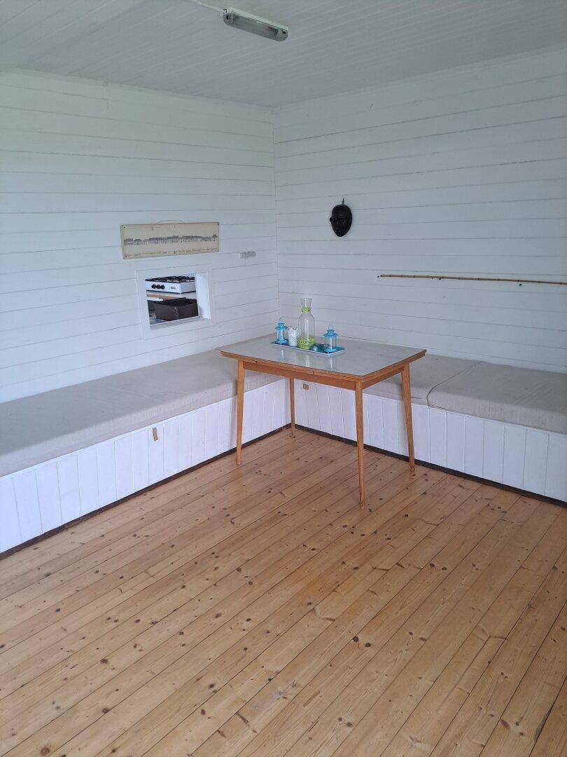 Wohnbereich mit eingebauten Sitzbänken, einem kleinen Tisch und Holzdielenboden.