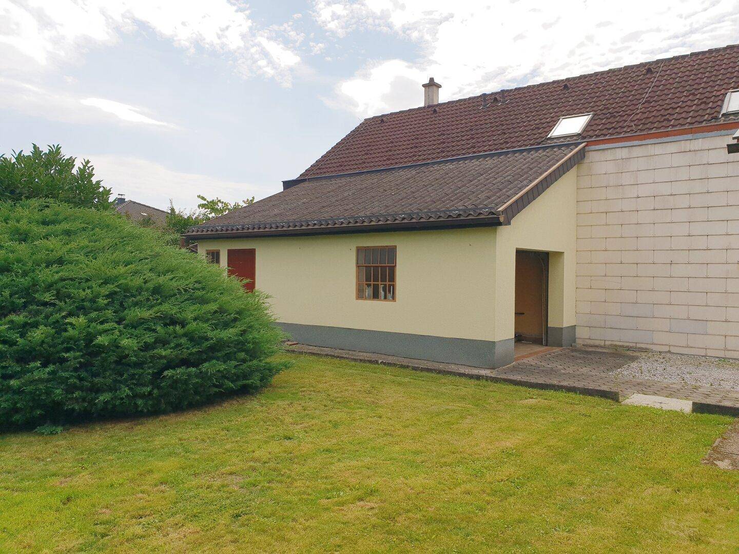 Rückseite des Hauses mit Rasenfläche und einem Anbau unter einem Satteldach.