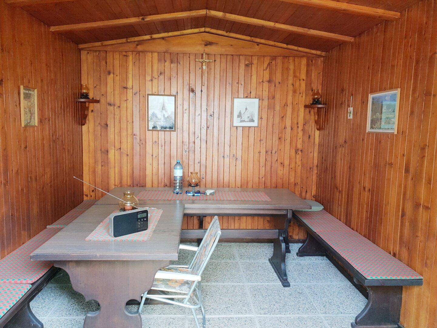 Gemütlicher Wintergarten mit Holztäfelung, Esstisch und Bänken.