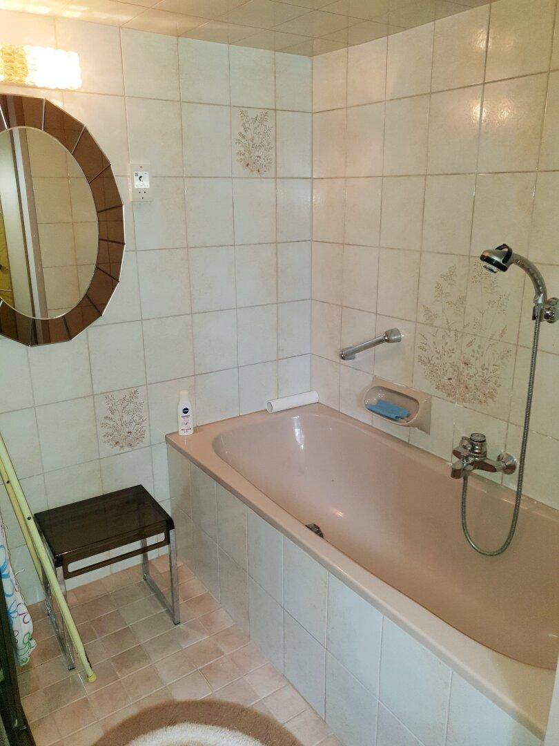 Badezimmer mit Badewanne, Duschvorrichtung und beigefarbenen Fliesen.
