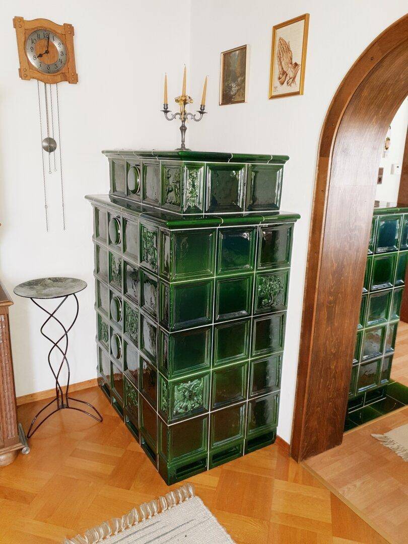 Detailansicht eines traditionellen grünen Kachelofens in einem Wohnbereich mit Parkettboden.