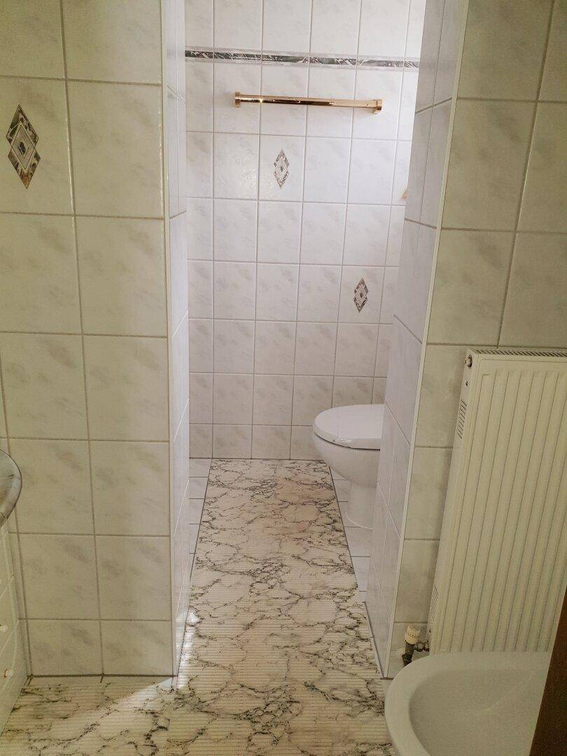 Kleines WC mit weißen Fliesen, gemustertem Boden und Heizkörper.