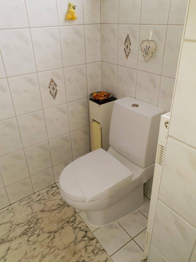 Nahaufnahme einer Toilette in einem gefliesten Raum mit Heizkörper.