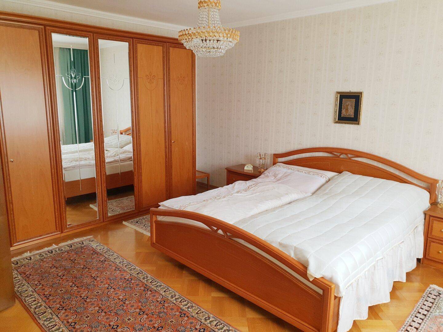 Helles Schlafzimmer mit Doppelbett, großem Spiegelschrank und Parkettboden.