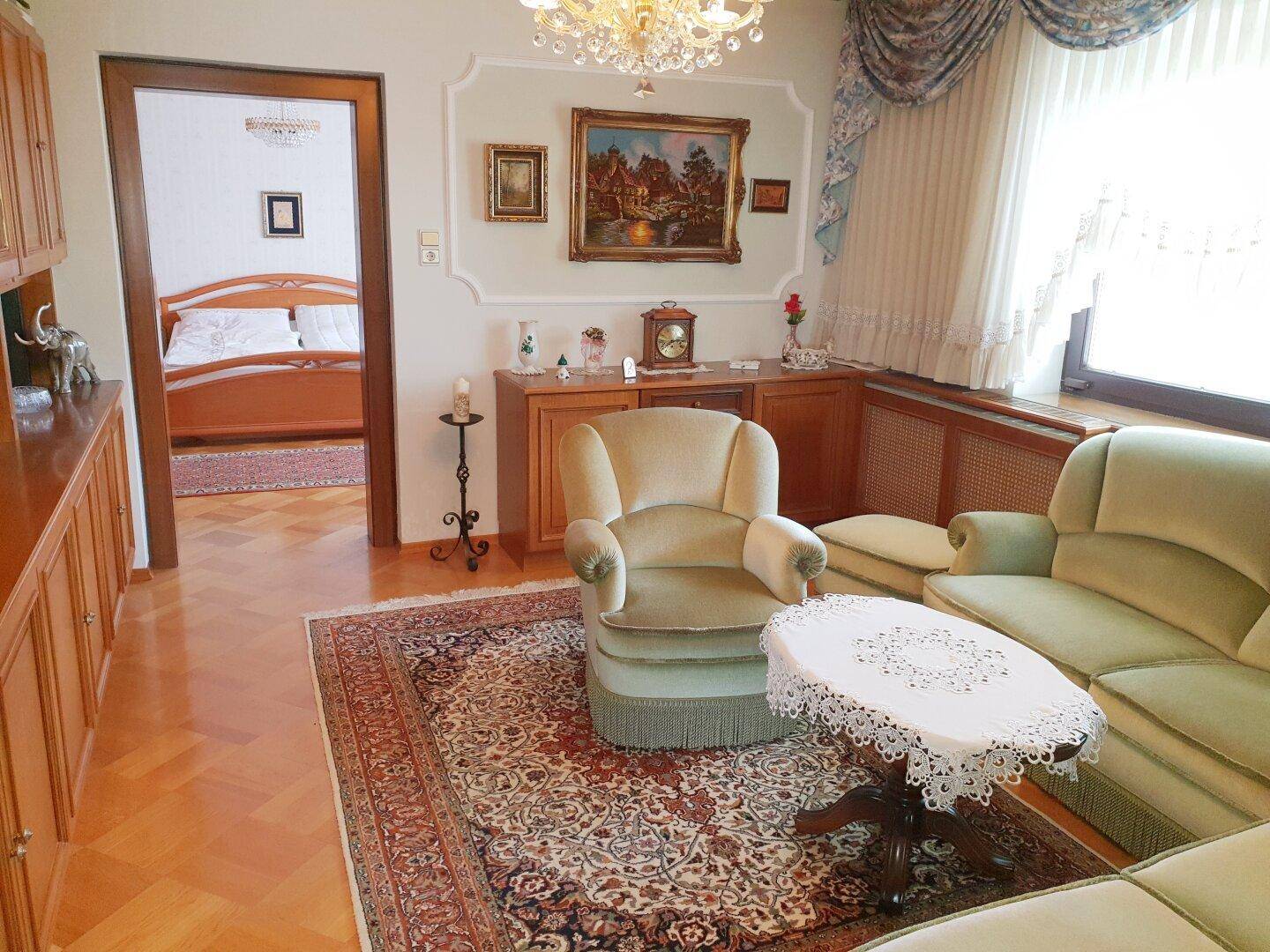 Gemütliches Wohnzimmer mit traditionellen Möbeln, Teppich und Blick ins Schlafzimmer.