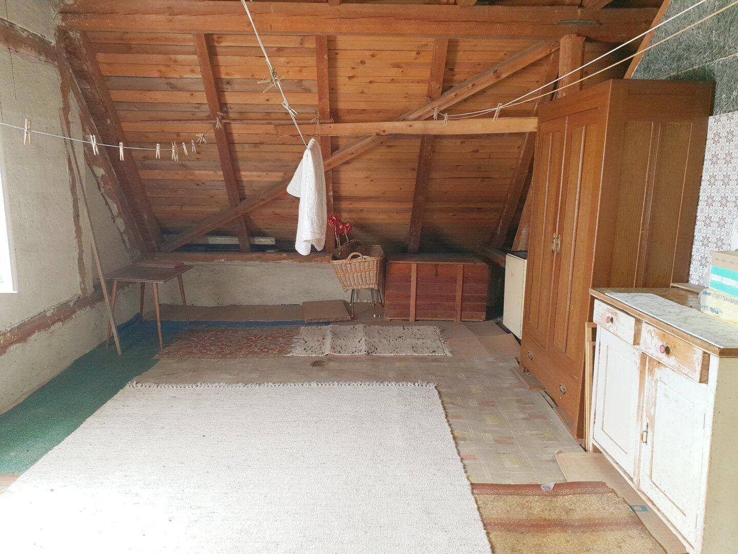 Dachboden mit sichtbaren Holzbalken, Teppichen und Stauraum.