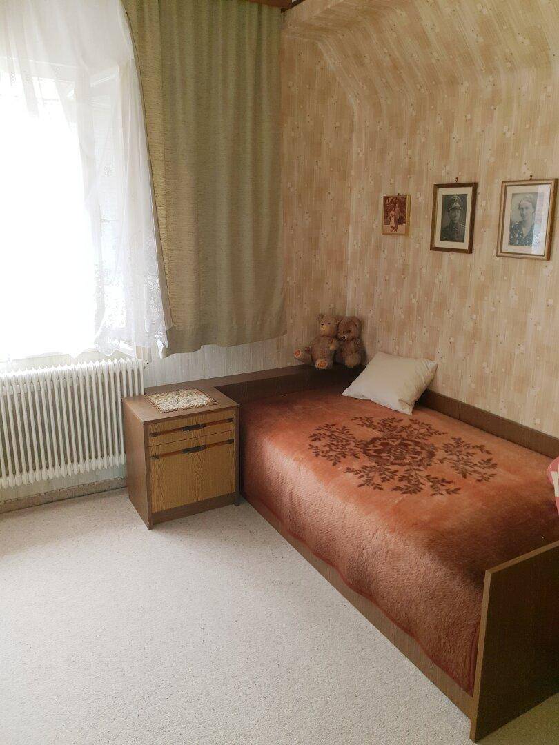 Gemütliches Schlafzimmer mit Einzelbett, Teppichboden und Fenster mit Heizkörper.