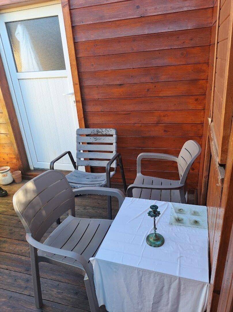 Gemütlicher Außenbereich auf einer Holzterrasse mit Tisch und Stühlen neben dem Eingang.