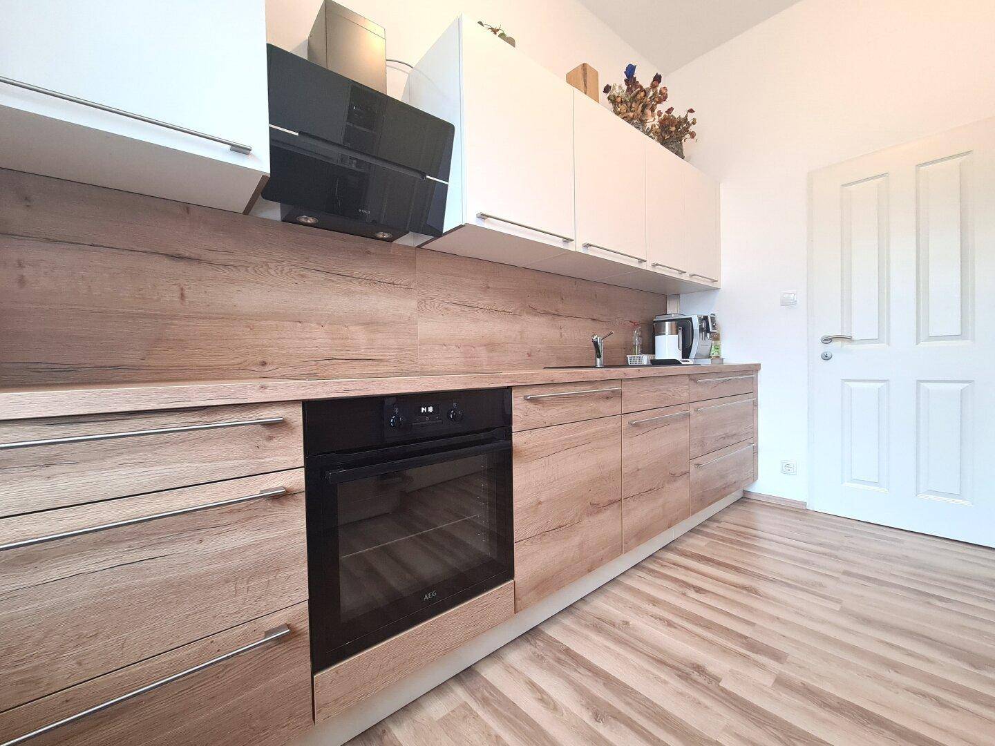 Moderne Küche mit Holzoptik-Arbeitsplatten, weißen Oberschränken und integriertem Backofen.