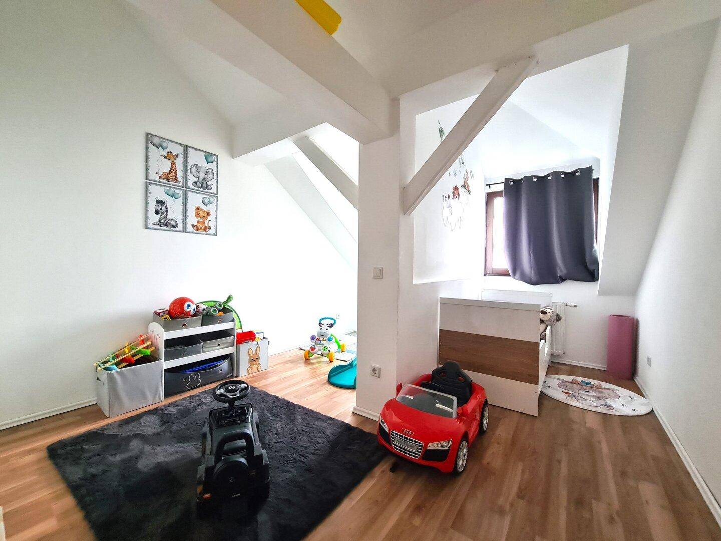 Helles Kinderzimmer unter Dachschräge mit Laminatboden, Spielzeug und sichtbaren Holzbalken.
