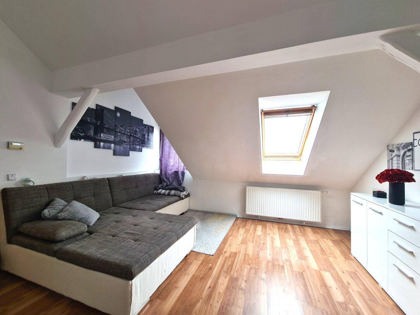 Gemütliches Wohnzimmer mit großem Sofa, Laminatboden, Dachschräge und einem Dachfenster.