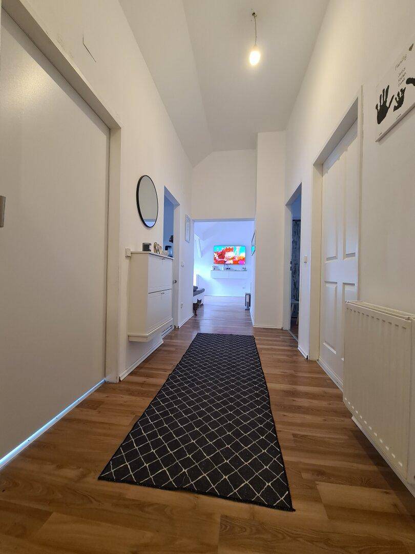 Heller Flur mit Laminatboden, Spiegel und Schuhschrank, der zu einem farbenfrohen Raum führt.