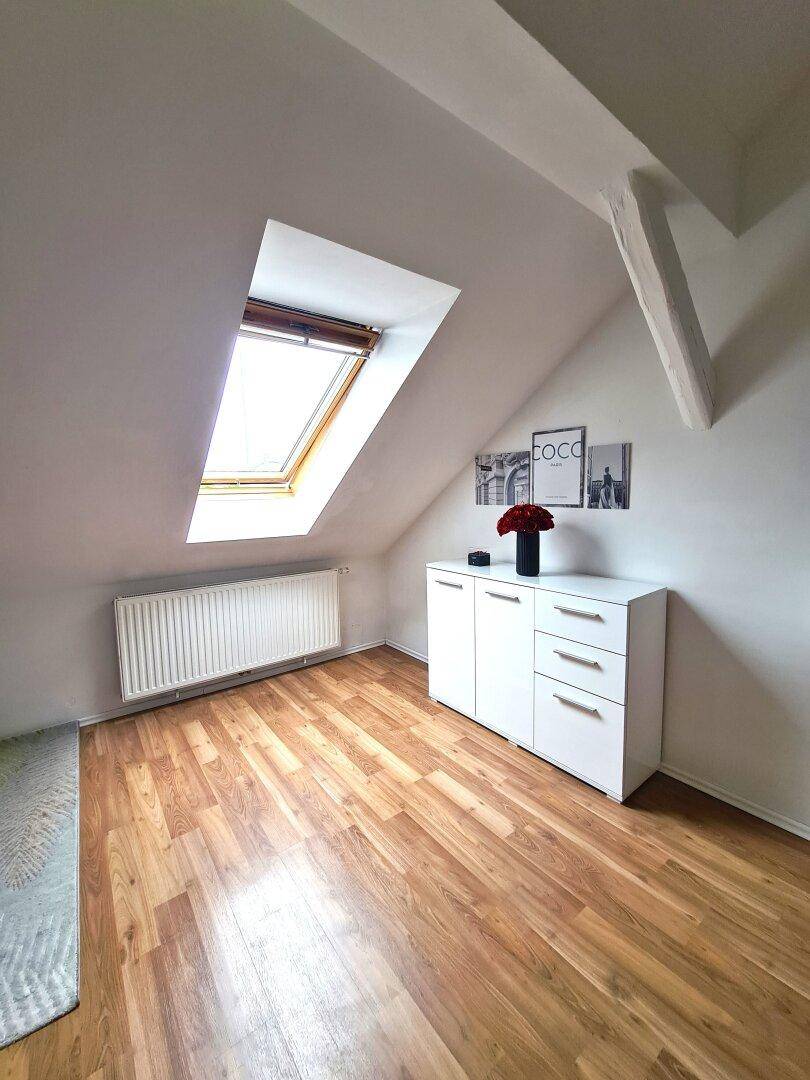 Heller Raum mit Laminatboden, weißem Schrank, Dachschräge, Dachfenster und Heizkörper.