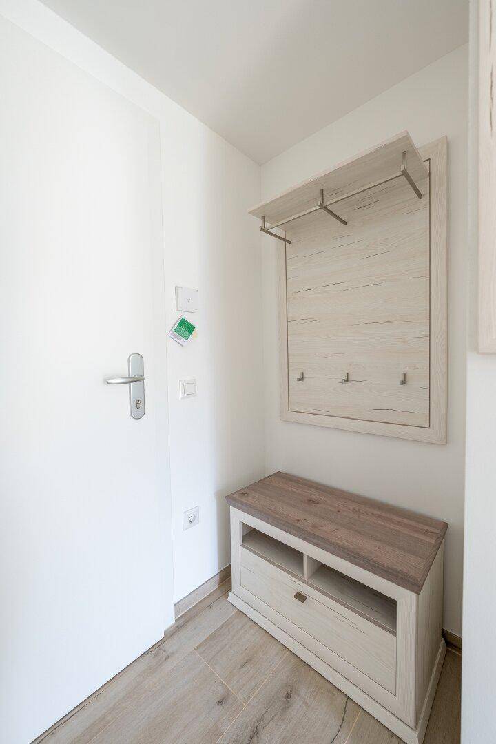 Heller Eingangsbereich mit Garderobe, Schuhbank und weißer Tür.