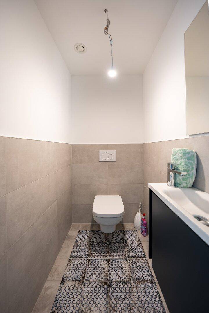 Modernes Gäste-WC mit Wand-WC, Waschtisch und dekorativen Bodenfliesen.