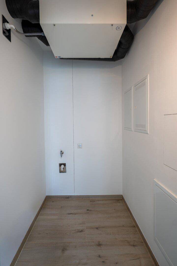 Hauswirtschaftsraum mit Anschlüssen für Waschmaschine und sichtbaren Lüftungsrohren.