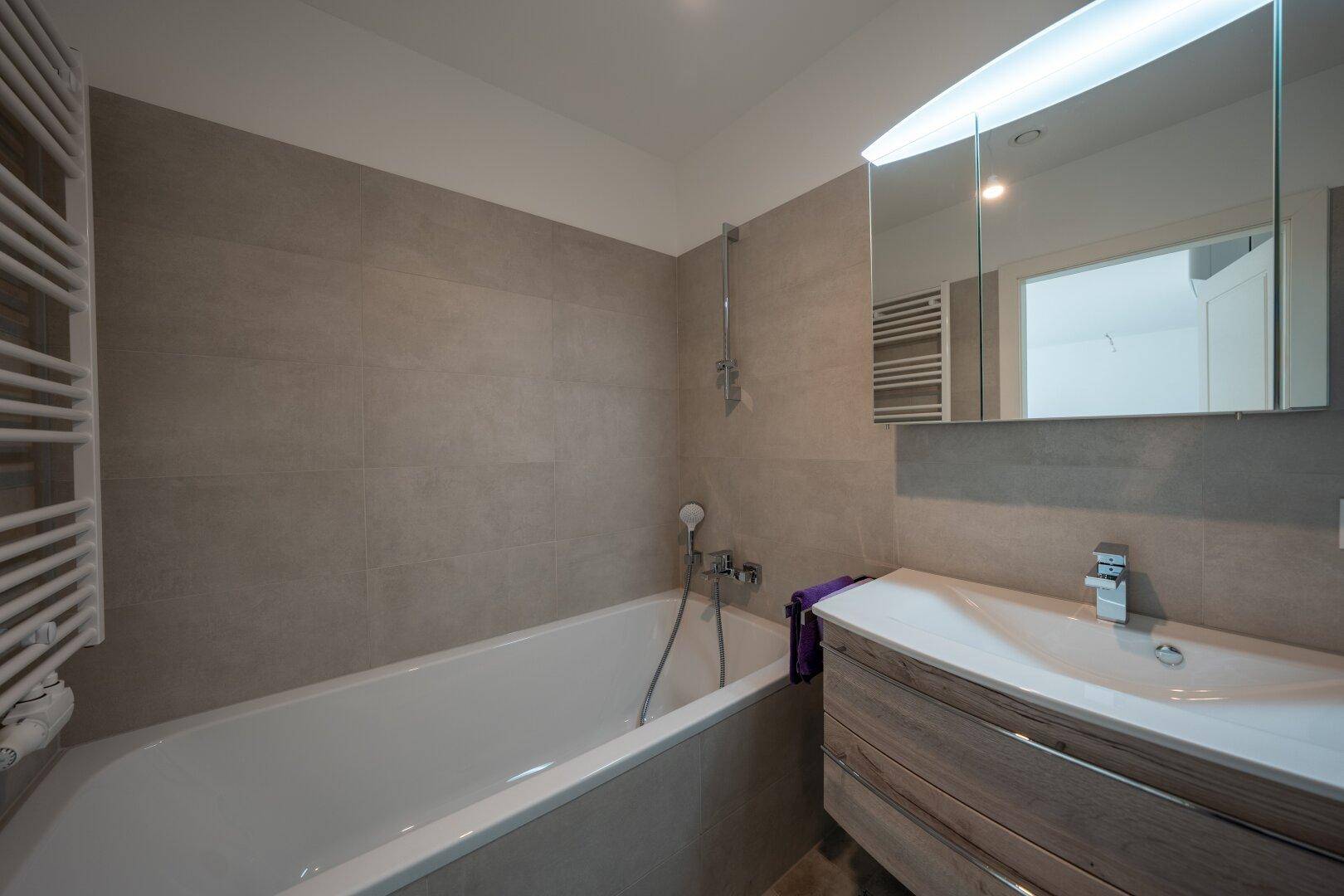 Modernes Badezimmer mit Badewanne, Holzwaschtisch, Spiegelschrank und beheiztem Handtuchhalter.