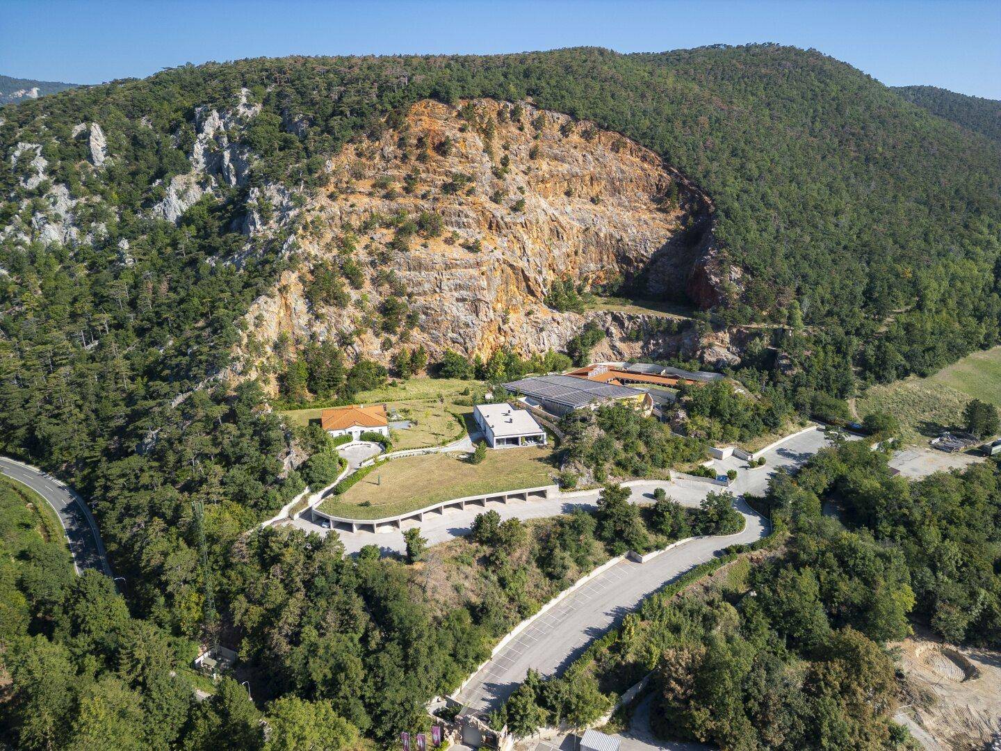 Weitläufige Luftaufnahme des Anwesens in einer bergigen Landschaft mit Straßen und viel Grün.