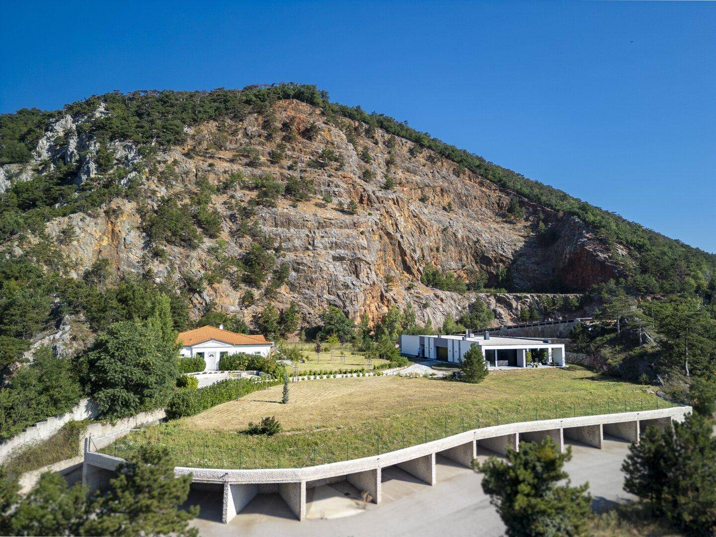 Gesamtansicht des Anwesens mit modernem und traditionellem Haus sowie Tiefgarage vor dem Berg.