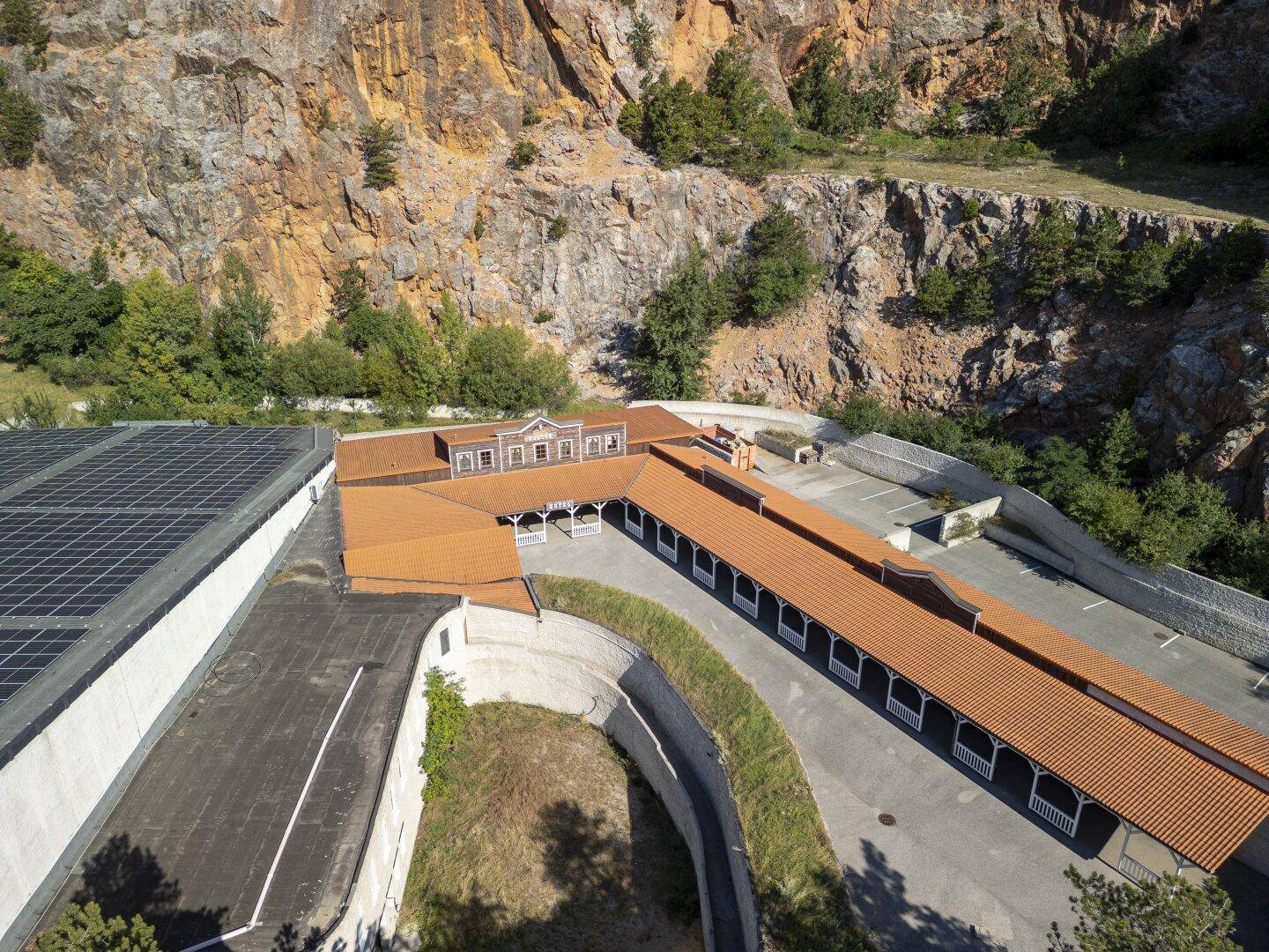Nahaufnahme eines Gebäudekomplexes mit Solaranlagen und überdachtem Gang vor der Felswand.