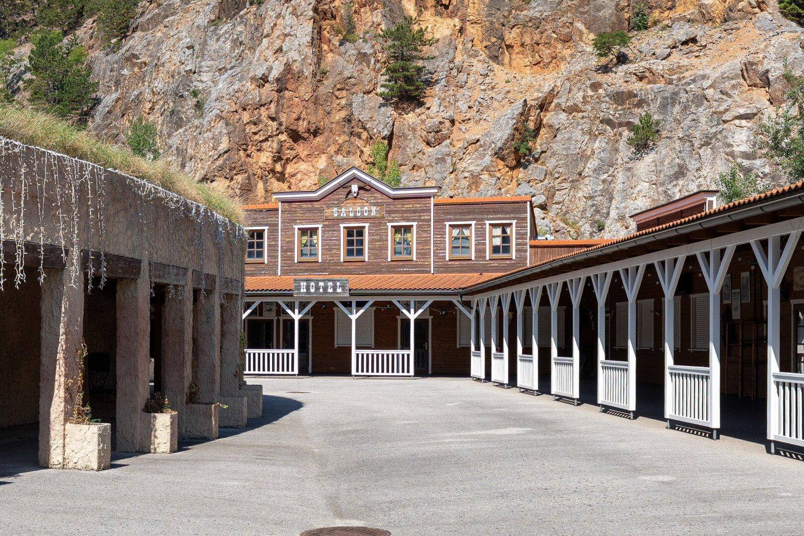 Außenansicht eines Gebäudekomplexes im Wild-West-Stil mit Hotel und Saloon vor Felswand.