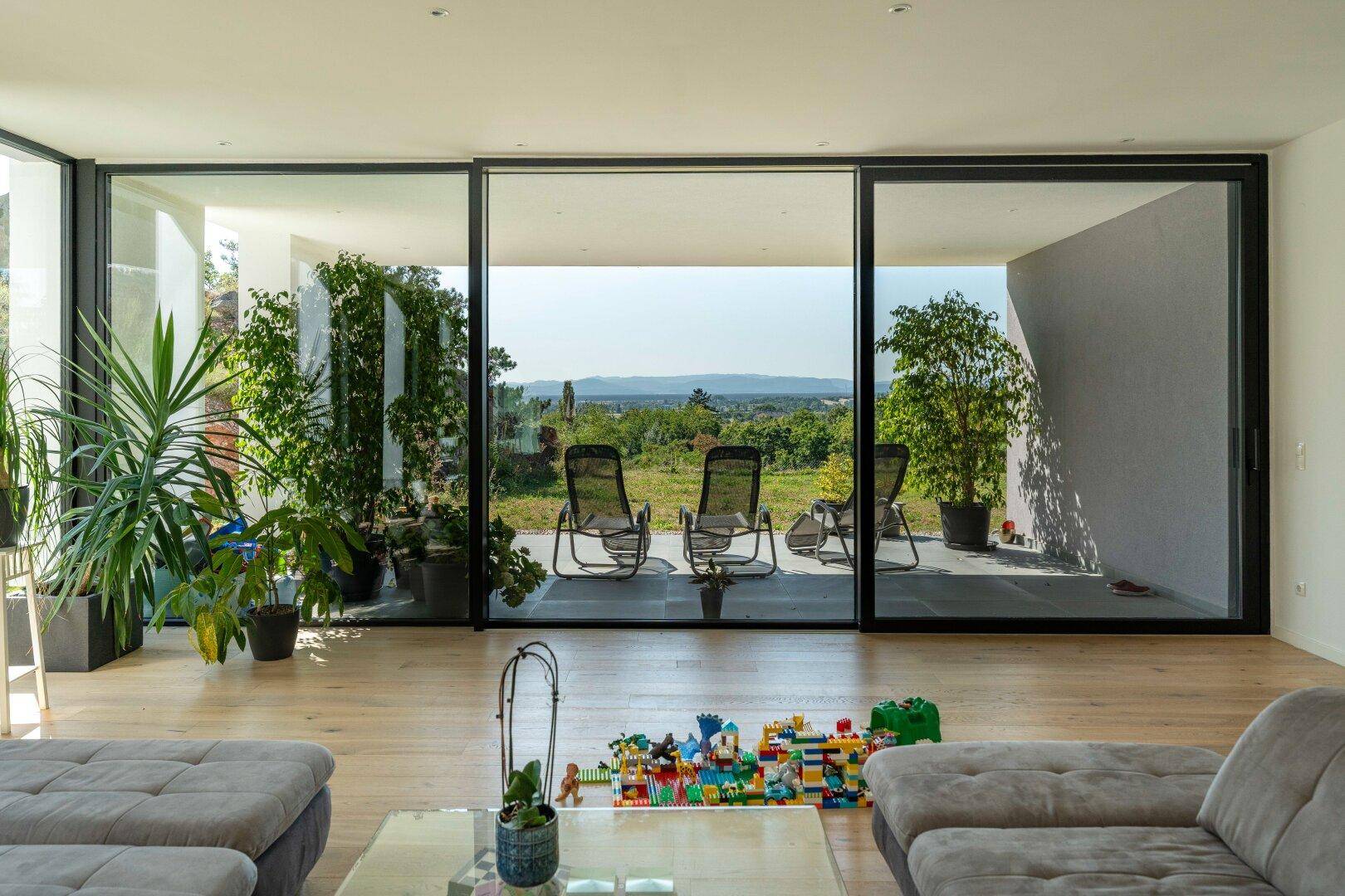 Helles Wohnzimmer mit großen Glasschiebetüren, Holzboden und Blick auf die Landschaft.