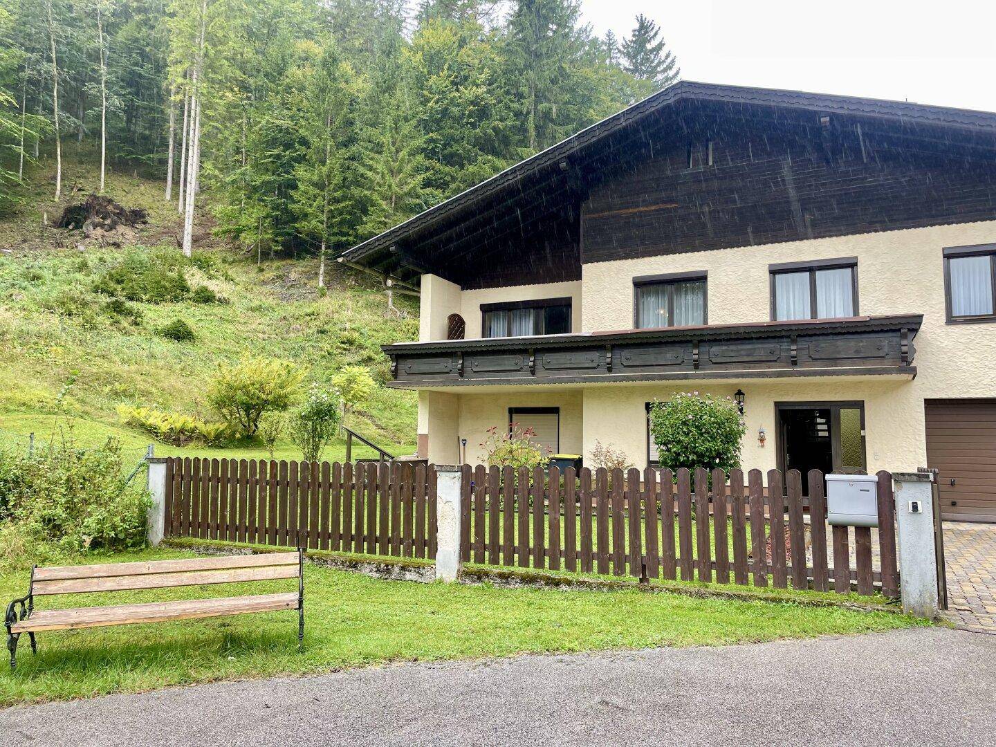 Hausfassade mit traditionellen Holzelementen und Blick auf den bewaldeten Hang.