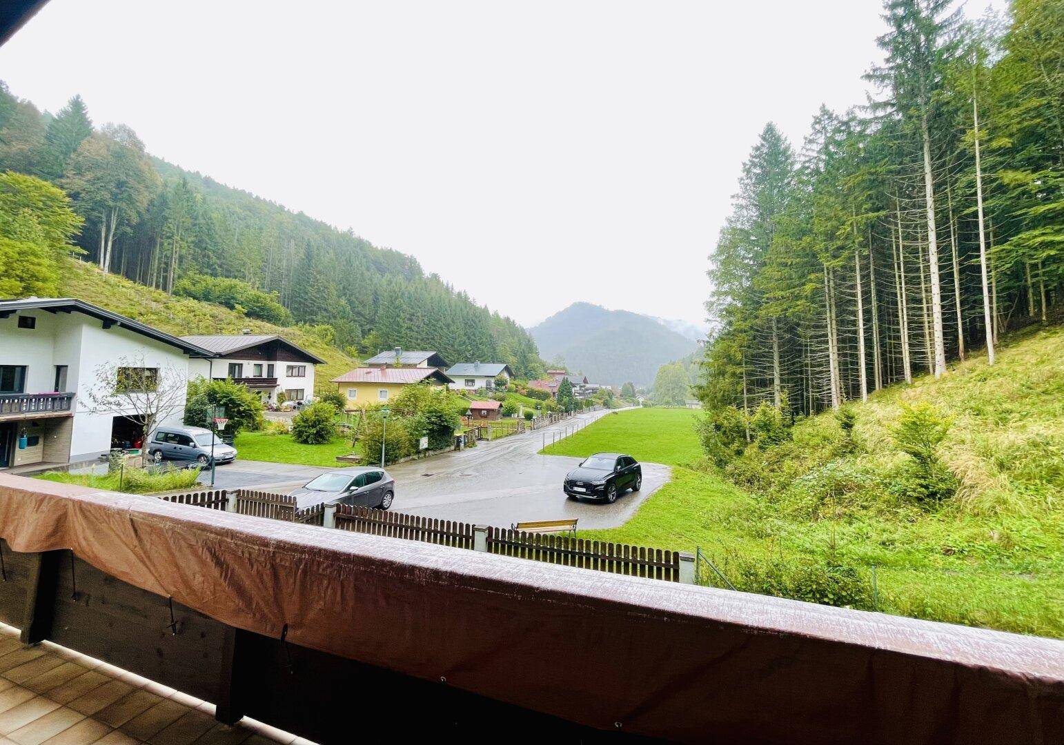 Blick vom Balkon auf die umliegende Berglandschaft und das Tal mit weiteren Häusern.