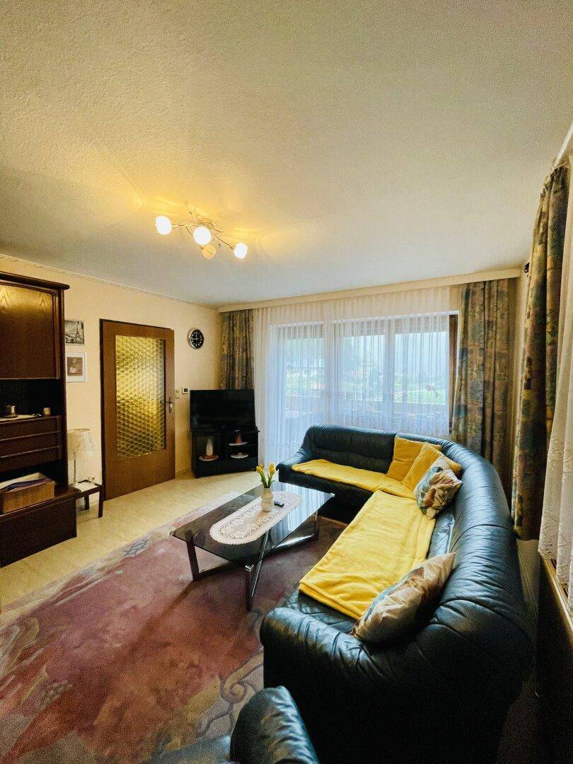 Geräumiges Wohnzimmer mit großer Ledercouch, Teppichboden und Blick ins Grüne.