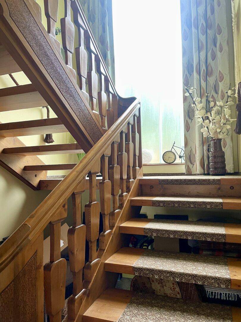 Holztreppe mit Teppichläufern und einem Fenster, das den Bereich erhellt.