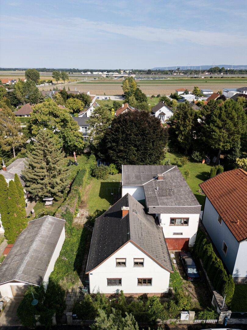 Luftaufnahme des Hauptgebäudes mit zwei Dachformen, umgeben von Bäumen und Gärten.