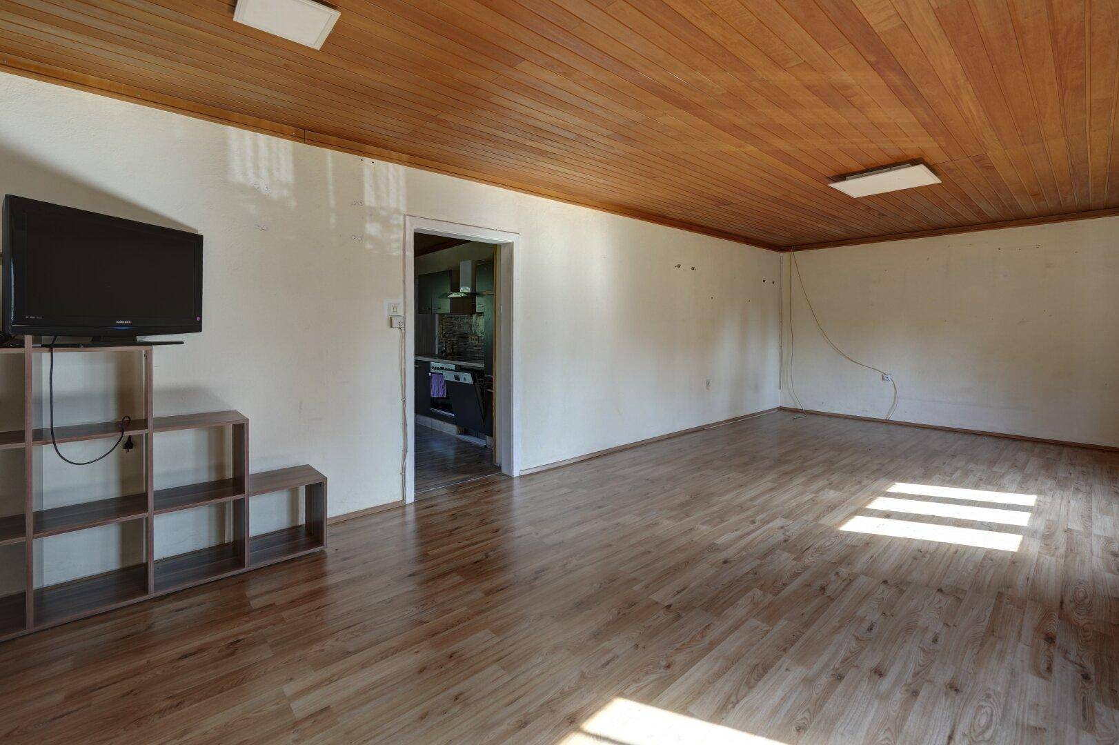 Geräumiges Wohnzimmer mit Holzdeckenverkleidung, Laminatboden und viel natürlichem Licht.