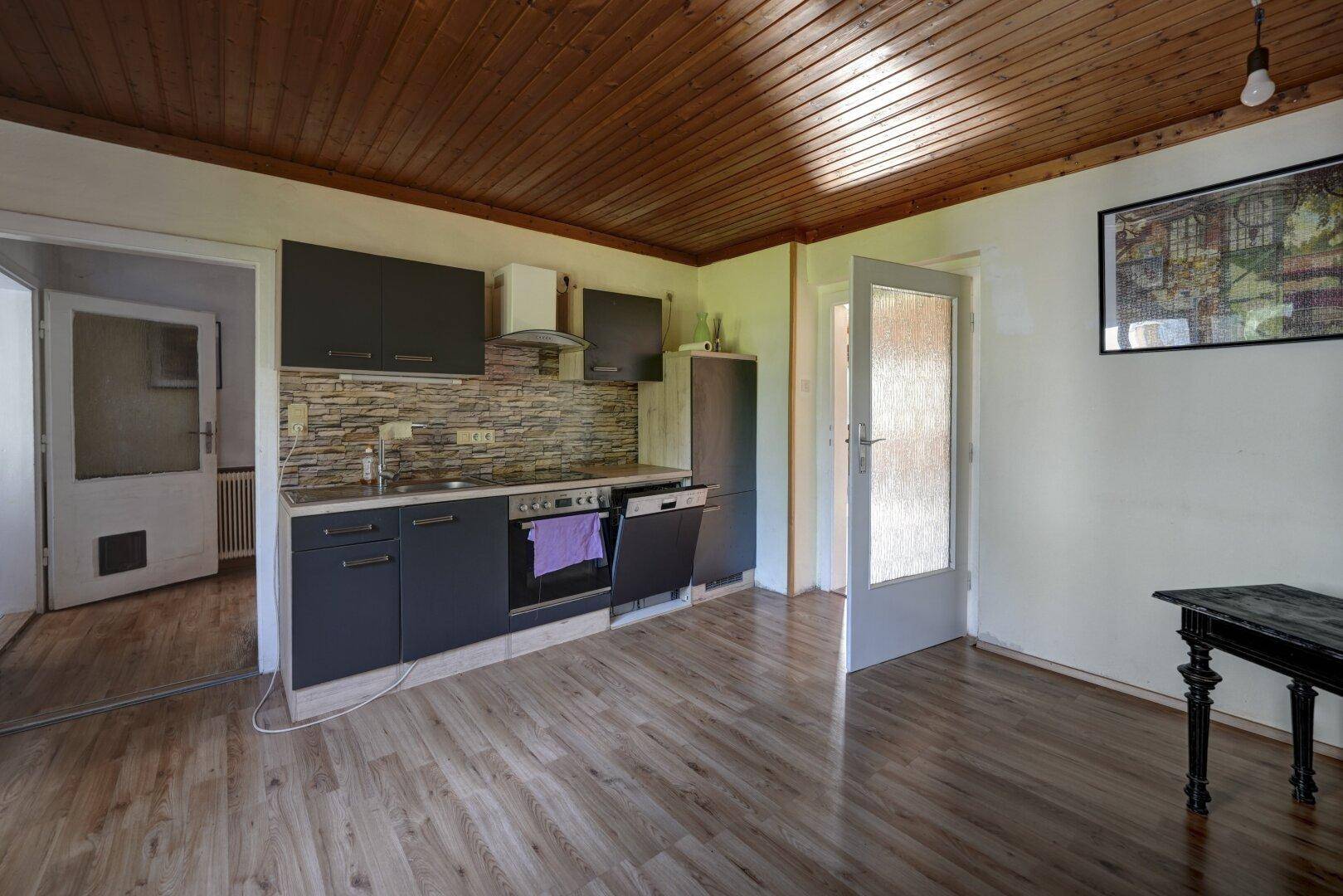 Funktionale Küche mit dunklen Schränken, Steinoptik-Rückwand und Holzdeckenverkleidung.