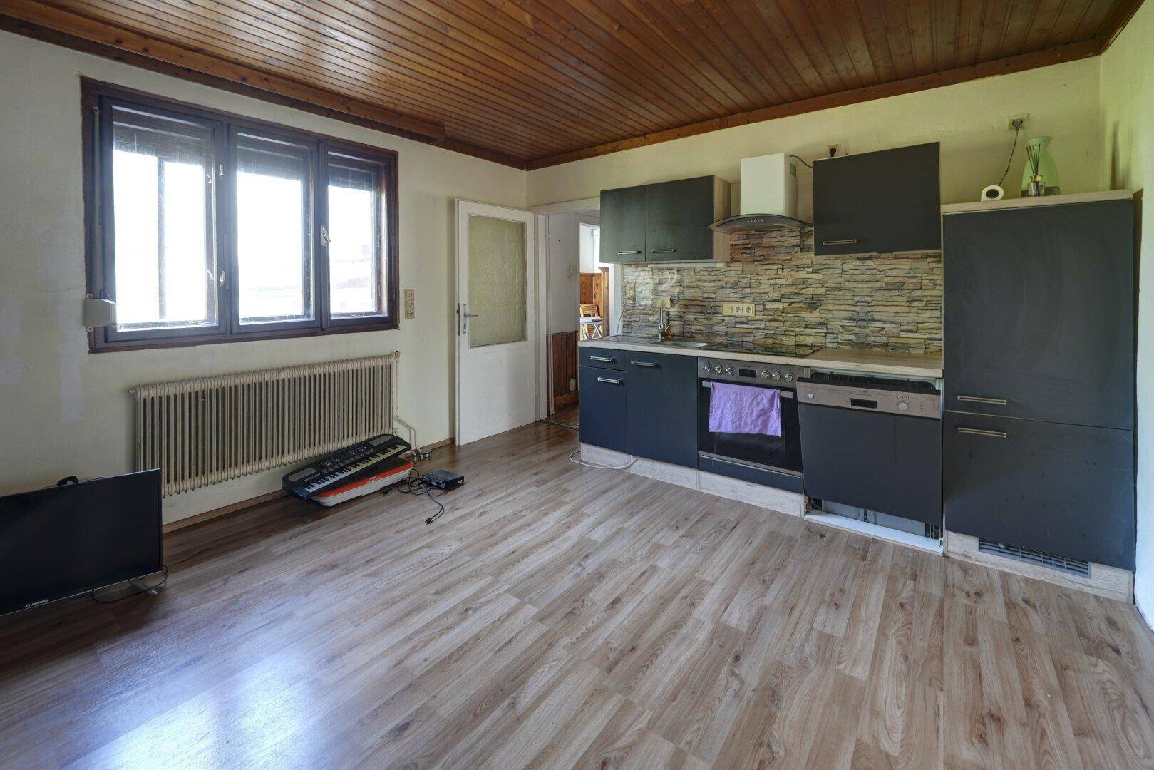 Helle Küche mit Fenster, Heizkörper und moderner Einbauküche in dunklem Grau.
