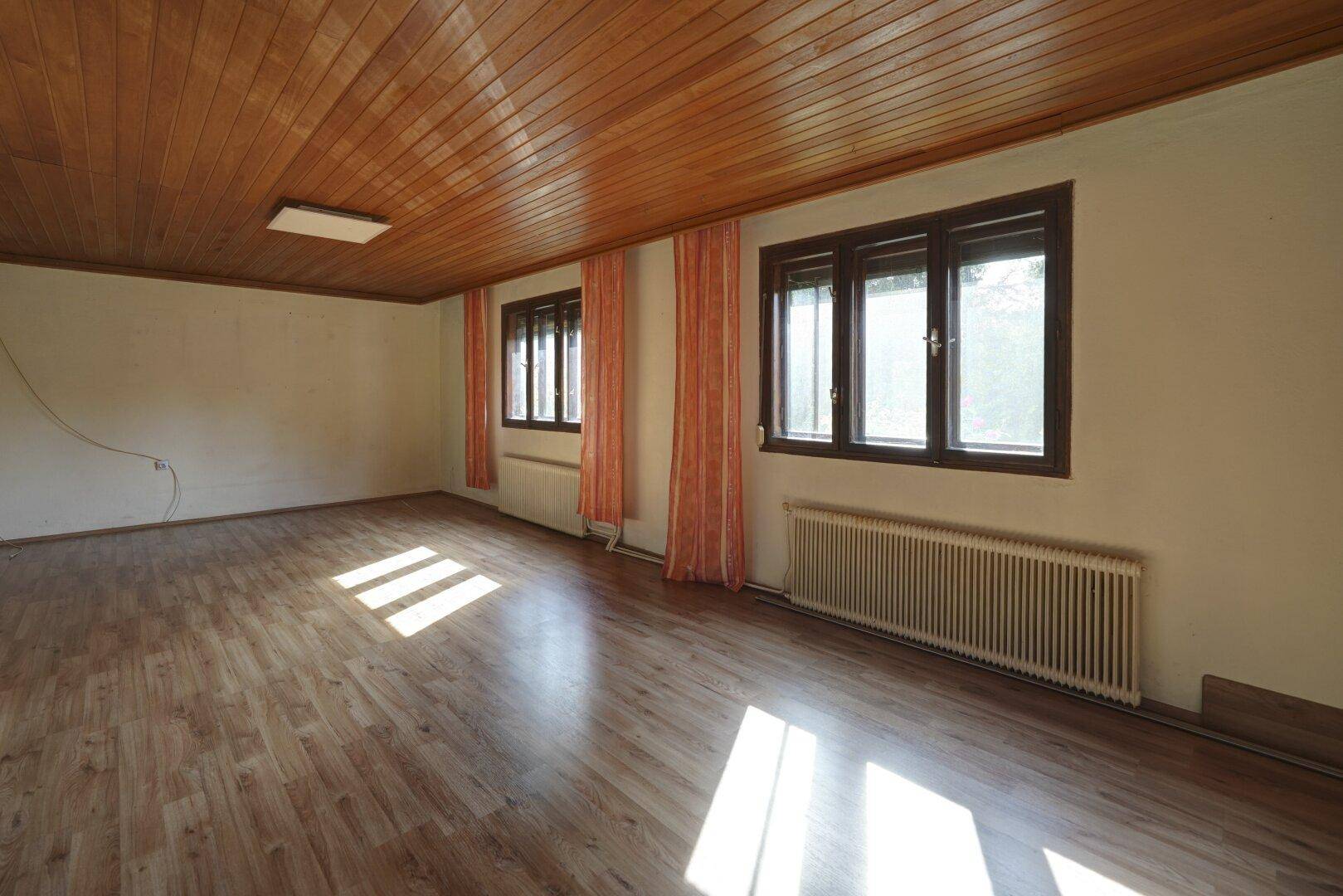 Helles Zimmer mit Holzdeckenverkleidung, Laminatboden und großen Fenstern für viel Licht.