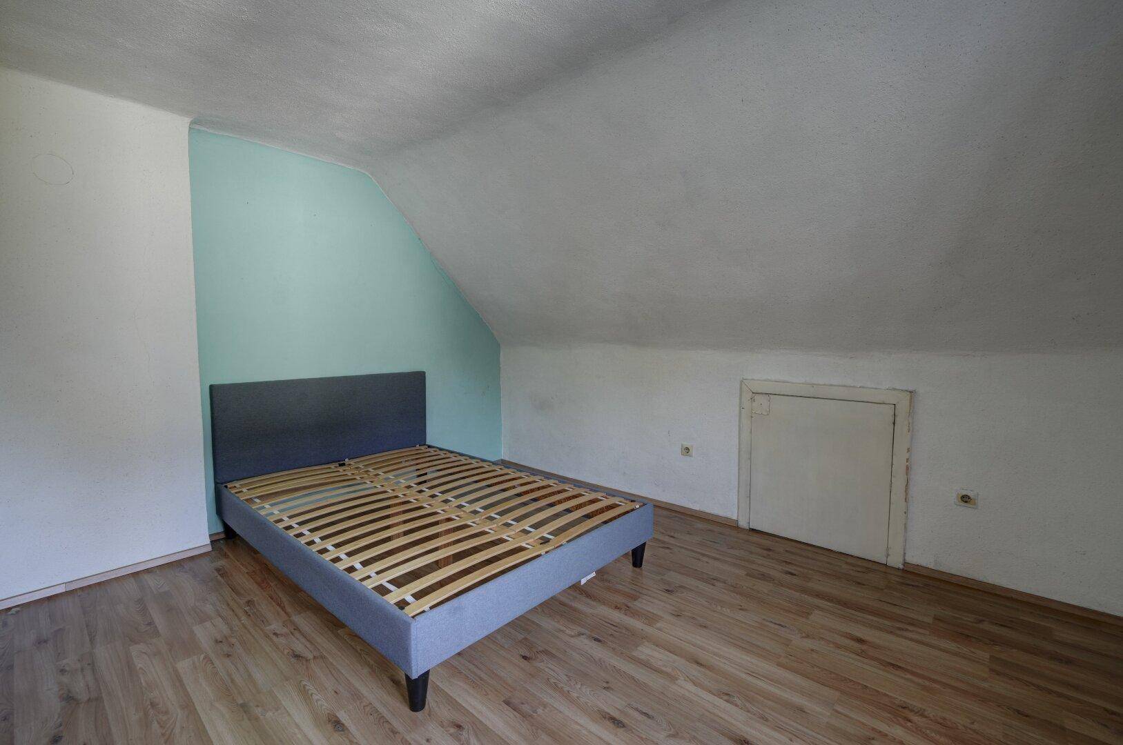 Gemütliches Schlafzimmer im Dachgeschoss mit schräger Decke und Laminatboden.