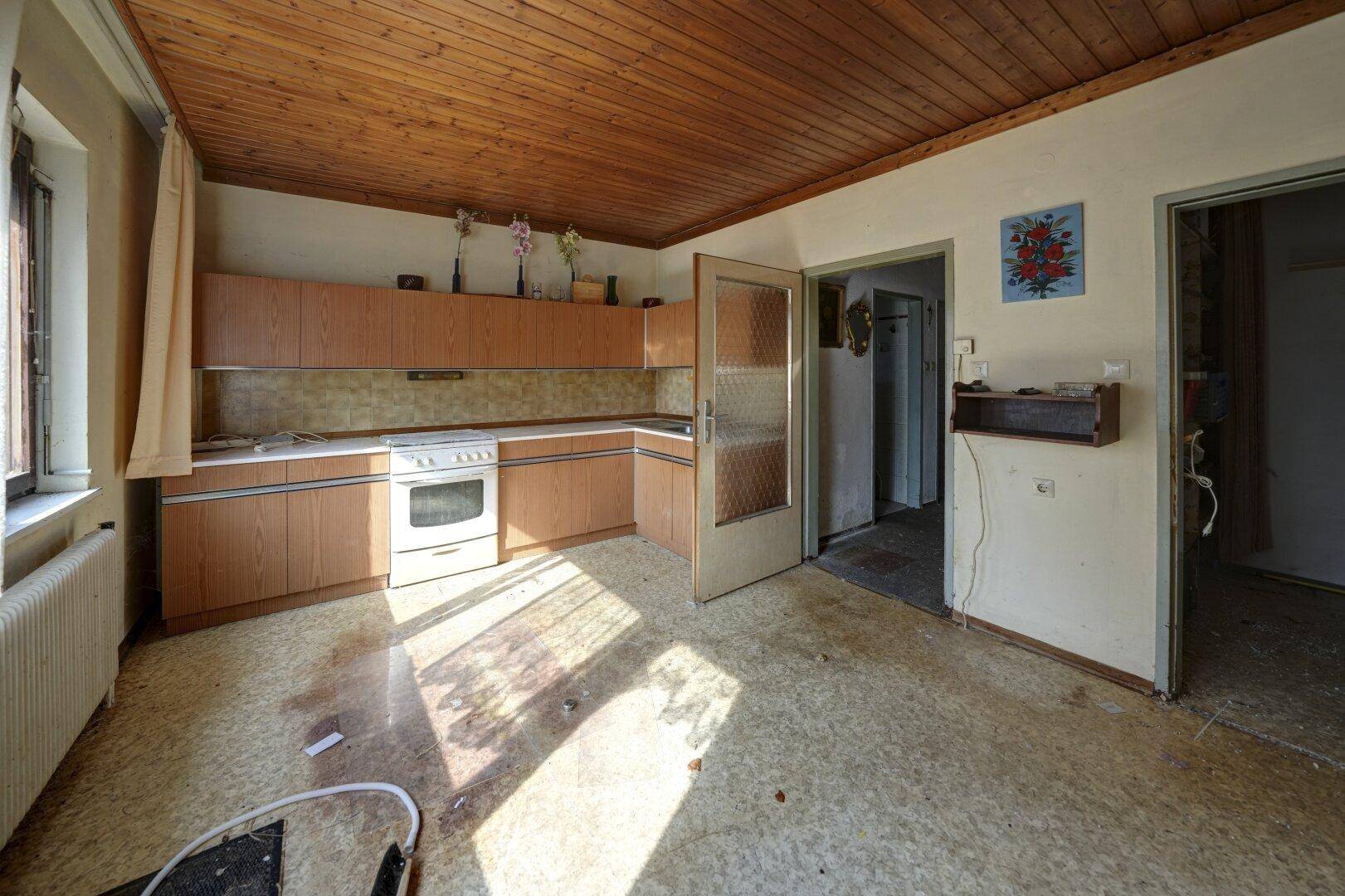 Ältere Küche mit Holzschränken, einem Herd und Linoleumboden, renovierungsbedürftig.
