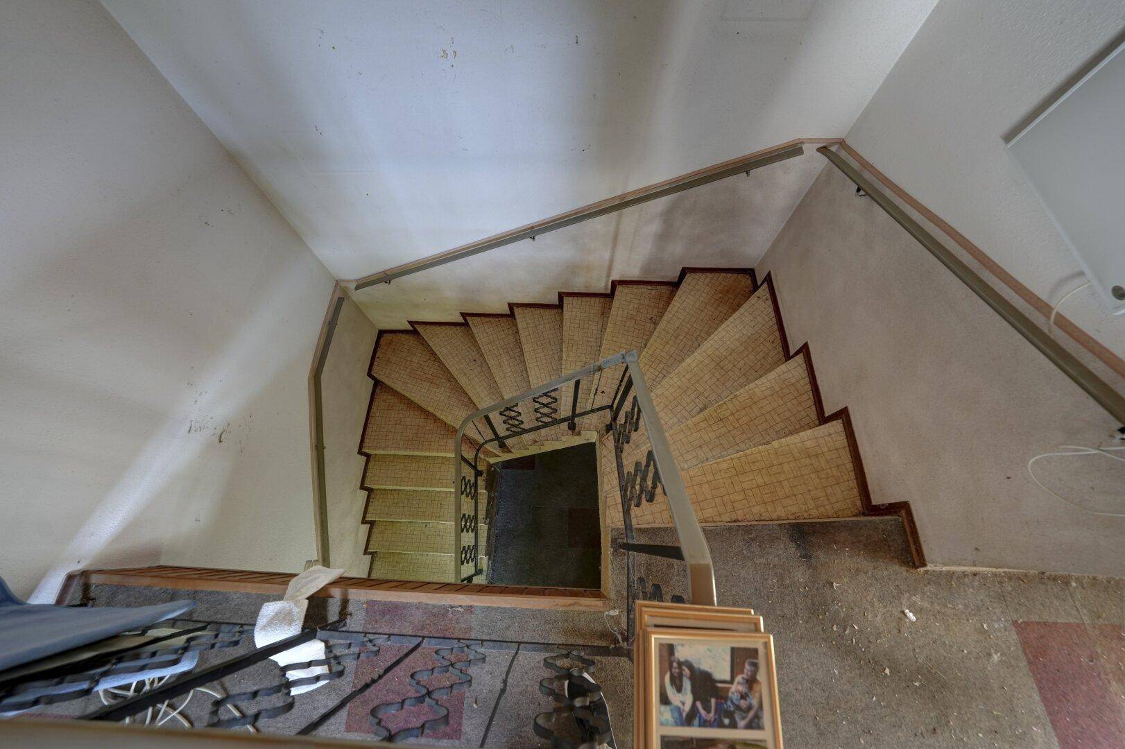Wendeltreppe mit gefliesten Stufen und einem schmiedeeisernen Geländer, die in die Tiefe führt.